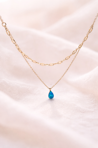Gold necklace with a blue teardrop pendant on a soft pink background